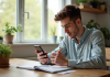Jeune adulte gérant ses finances avec smartphone et carnet